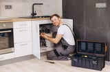 Professional plumber working on installing or repairing water filter system under sink