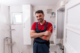 A plumber stands confidently in a stylish bathroom, holding a wrench and ready to assist with repairs during a home service visit