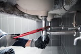 Plumber uses wrench to repair water pipe under sink